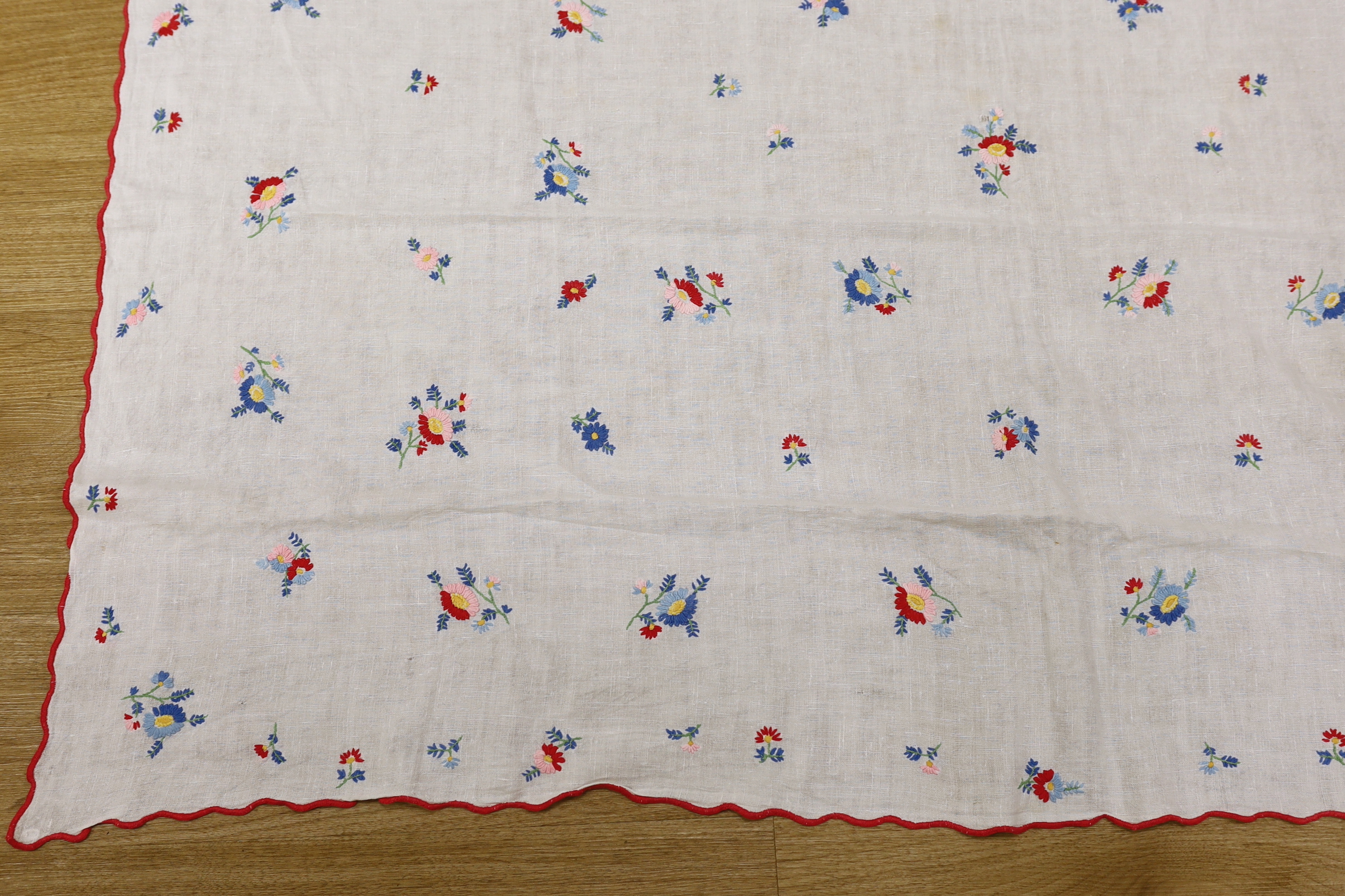 A 20th century woven linen panel, hand embroidered with scattered floral polychrome sprigs and a scalloped red buttonholed embroidered edge, possibly Swiss, 153 x 100cm